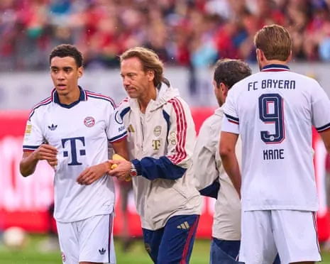 Jamal Musiala is helped from the field by a Bayern Munich doctor after falling to the ground during their game at Heidenheim.